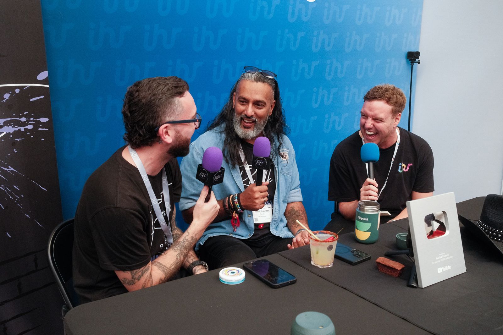 Three podcast guests laughing around a table of microphones